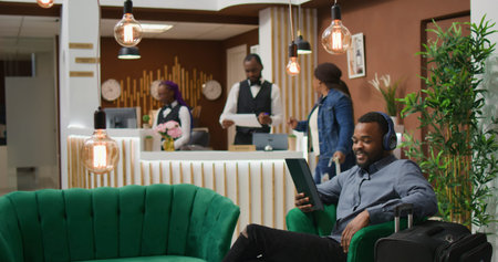 Man on videocall conference in hotel lobby, calling family and friends to discuss about travelling on holiday while he waits for room registration.
