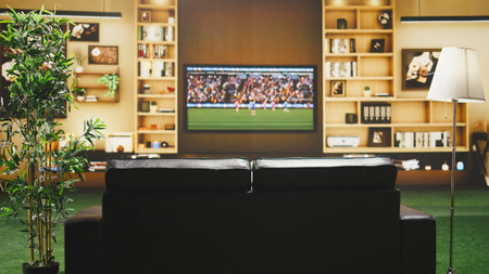 Soccer game broadcasted on TV in empty apartment living room before fans arrive. Cozy sofa, plant and television set screen creating comfortable home viewing setup for sports event