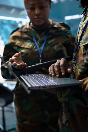 Close up of military officers checking intelligence intel on laptop in command center. Army team compares notebook data with satellite maps and target information, doing brainstorming