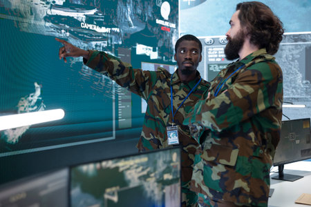 Soldier shows enemy targets on surveillance map to military officer in command center. Army specialist points at tracked targets and operation data on large display, providing intel