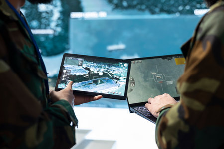Military personnel compare target information on tablets in command center. Army team colleagues check tactical surveillance imagery across devices screens