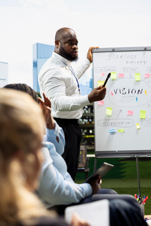 Business presenter explaining vision board with sticky notes and ideas during outdoor strategy workshop, informal meeting discussion with coworkers. Whiteboard presentation.