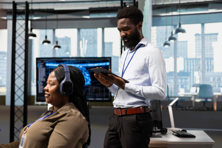 Technician developing applications using tablet, integrating AI next to office coworkers. IT specialist debugging applications with device using artificial intelligence in tech startup
