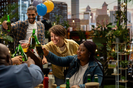 Adults raising bottles toward center of rooftop barbecue gathering, illustrating cheerful celebratory toast, social connection, celebration and shared leisure.