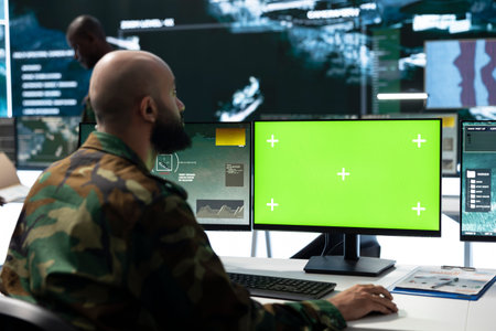 Green screen PC monitor used by army operator to devise defense intelligence strategy. Military unit coordinates operation in control room using mockup computer, close up