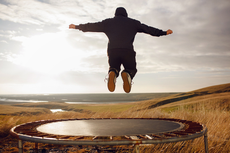 Back view of a high jump of a young man in outdoors on clear sky and sun, landscape background. lifestyle, freedom, happiness, emotional concept. Horizontal outside shot.の写真素材