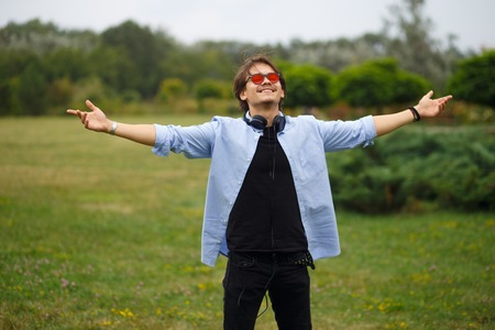 Happy youth boy with raised hands and red sunglasses sitting in park, feelings happiness. Freedom, emotional concept.の写真素材