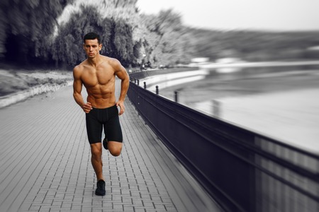 Moving, black and white image. Young athletic, fit, muscular man with naked torso, running morining in park, isolated on summer nature background. Horizontal view.の写真素材