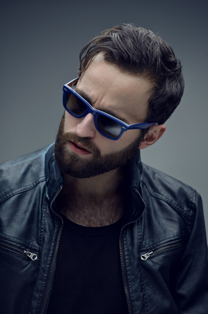 Profile portrait of a bearded brutal man in sunglasses and leather jacket, isolated on a dark grey background. Confident style.の写真素材