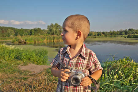 Little boy with a camera shooting evening landscapes near the lake
