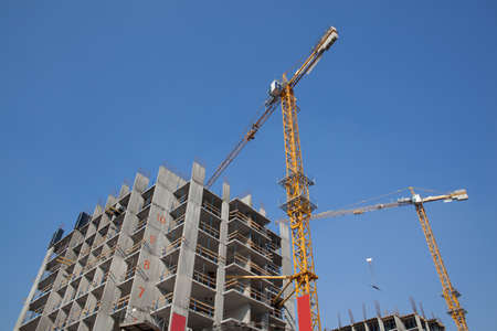 Two cranes developing modern residential buildings against blue skyの写真素材