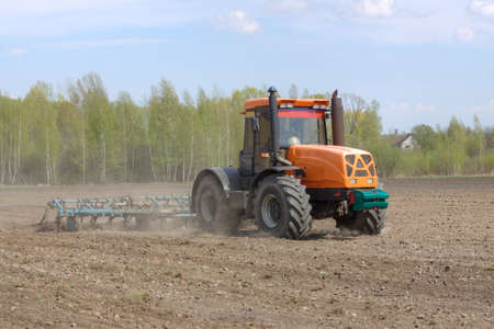 Tractor with a cultivator plowing the field in the springの写真素材