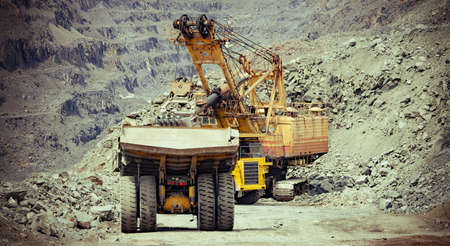 Heavy mining trucks and excavator working on the iron ore opencast mining siteの写真素材