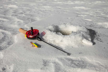 Ice fishing rod and lure near the hole in the iceの写真素材
