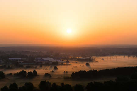 Sunset over the village in summer with fog in the valleyの写真素材