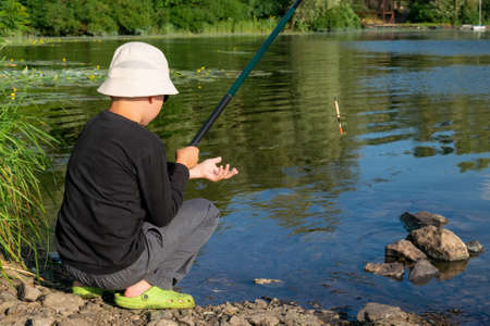 Young boy is adjusting his tackle on the fishing rodの写真素材