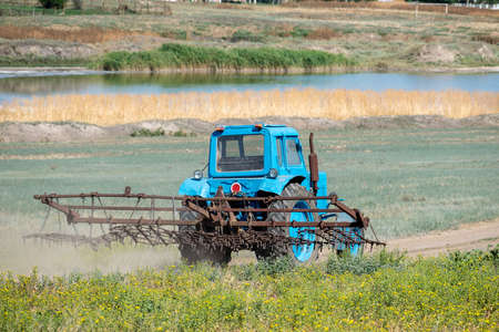 Old tractor with harrow is driving along the country roadの写真素材