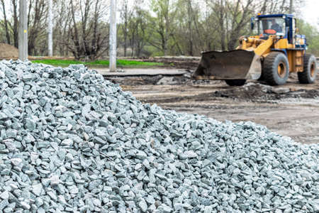 Road repair works - tractor is removimg old pavement and fresh gravel on the foreground