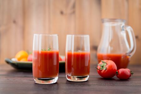 Glass of tomato juice with vegetables on old wooden background, with greenery and tomatoesの写真素材