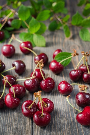 fresh red cherries on an old wooden table with green leaves, rustic styleの写真素材