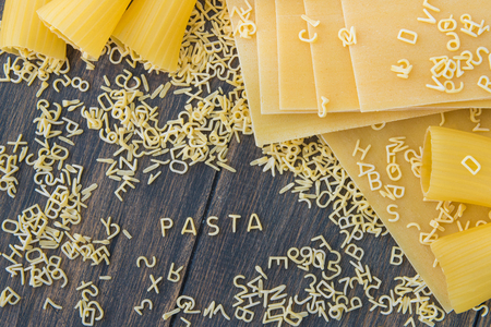 Uncooked raw pasta alphabet yellow letters with macaroni and lasagna on a black wooden rustic background top viewの写真素材