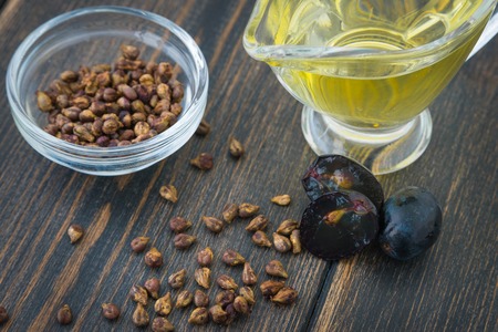 A glass oiler of natural grapeseed oil and grape seeds on black wooden backgroundの写真素材