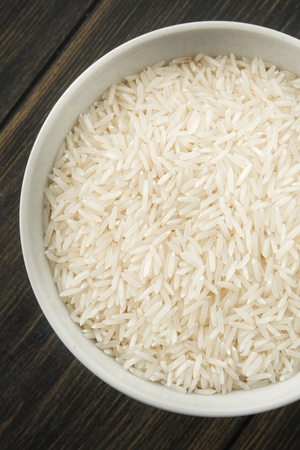 Raw Basmati rice in white porcelain bowl on dark wooden background top viewの写真素材