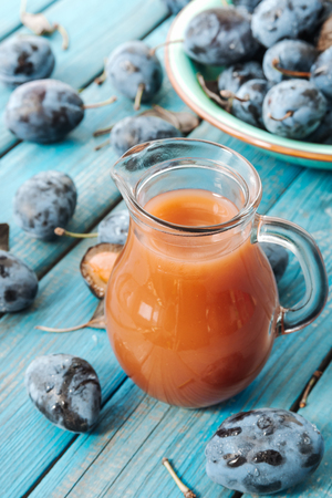 A glass decanter of fresh Damson plum juice on a blue rustic wooden background close-up.の写真素材