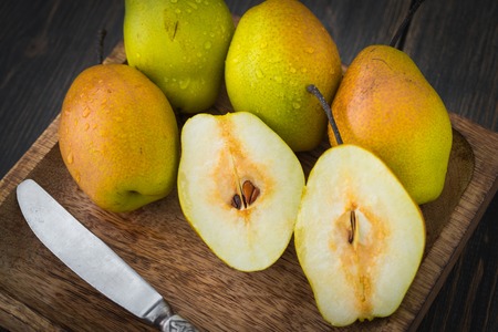 Sliced pears of different ripeness in brown craft wooden plate on dark rustic wooden background close-upの写真素材