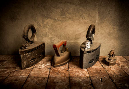 Old, antique cast irons on tiles with concrete wall background. Vintage house appliances.の写真素材