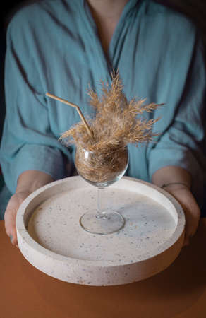 Girl dressed in kimono holding pampas grass cocktail in a glass with a straw made of pampas stem on a plate. Minimal abstract composition background. Japandi interior idea. Refreshment idea.の写真素材