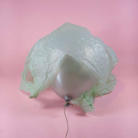 Plastic bag wrapped around grey balloon on soft pink background. Abstract pollution and environmental protection concept.の写真素材