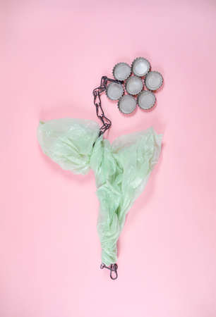 Flower made of rusty chain, plastic bag and bottle caps. On soft pink background. Minimal abstract...