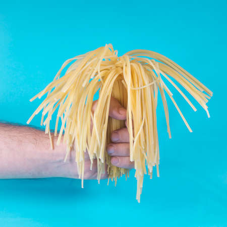 Hand holding half cooked spaghetti like a flower bouquet. Turquoise blue background. Minimal abstract food idea. Valentines and gift concept. With copy space.の写真素材