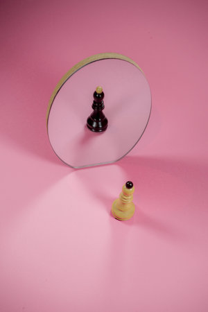 Chess piece white bishop with black reflection in a mirror. On trendy pastel pink background. Optical illusion. Minimal abstract different personalities idea.の写真素材