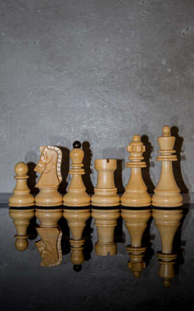 Wooden white chess pieces on dark mirror glass with concrete wall background. Games, sports and recreation idea. Minimal abstract intelligence and strategy concept.の写真素材