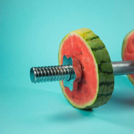 Weightlifting dumbbells made of steel bar and watermelon slices. On trendy pastel background. Training idea. Minimal abstract healthy nutrition, exercise, recreation and fitness concept. Copy space.の写真素材