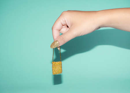 Hand with golden glitter nails holding miniature handbag. On trendy pastel blue background. Minimal abstract fashion and party concept.の写真素材