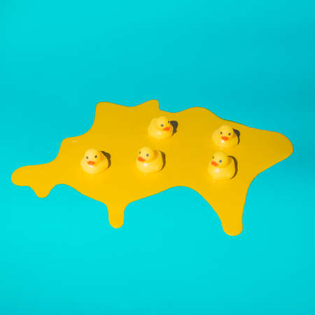 Five rubber ducklings swimming in melted yellow paint on trendy blue background. Minimal abstract...