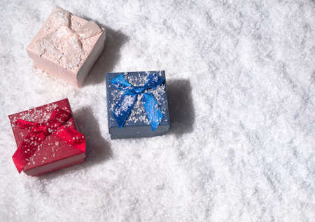 Red, pink and blue gift boxes covered in snow. Flat lay, top view. Minimal winter holidays concept. With copy space.の写真素材