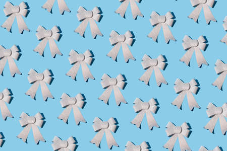 Sparkly silver bow ribbon pattern on pastel blue background. Christmas and New Year decoration idea....