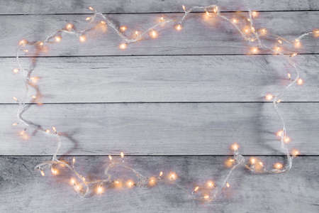 Creative winter holidays layout. Christmas tree lights framing light wooden boards. Flat lay, top view. Minimal New Year and Christmas concept. Copy space.の写真素材
