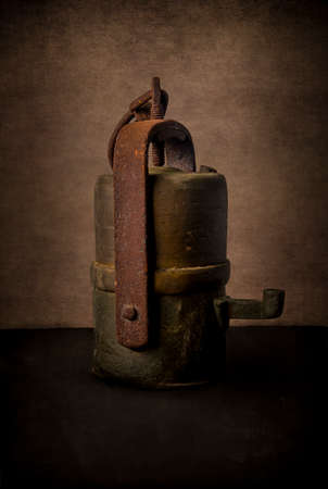 Still life with old gold digger lantern or carbide mining lamp, on grunge rustic background. Side view, cross light. Old tools and hard work concept.の写真素材