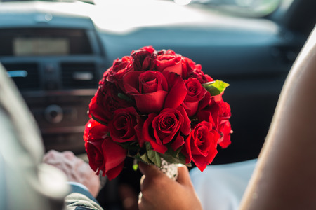 a detail shot of a beautiful bridal bouquet of red roses, held by the bride while driving in a carの写真素材
