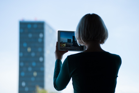 beautiful young blonde photographing modern architecture by using a tablet
