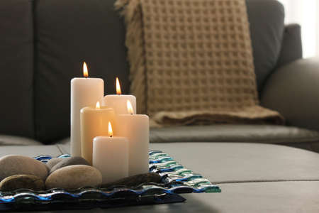Burning candles, pebbles, glass and gray sofa with blanket background. Interior decoration, living room.の写真素材