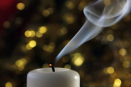 Extinguished candle with smoke on green twinkling lights on the background.の写真素材