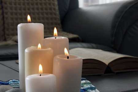 Burning candles, pebbles, glass tray, open book in gray sofa with blanket background. Interior decoration, living room.の写真素材