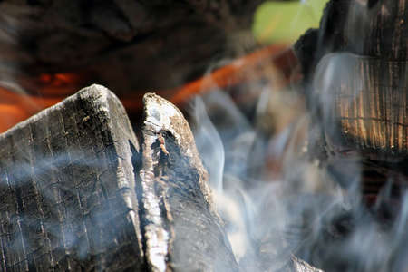 Burning firewood in the bonfire. Flames burning in the grill with smoke. Texture of fire and flame, dark background.の写真素材