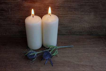 Two white candles burning on old wooden background with flower twig.の写真素材